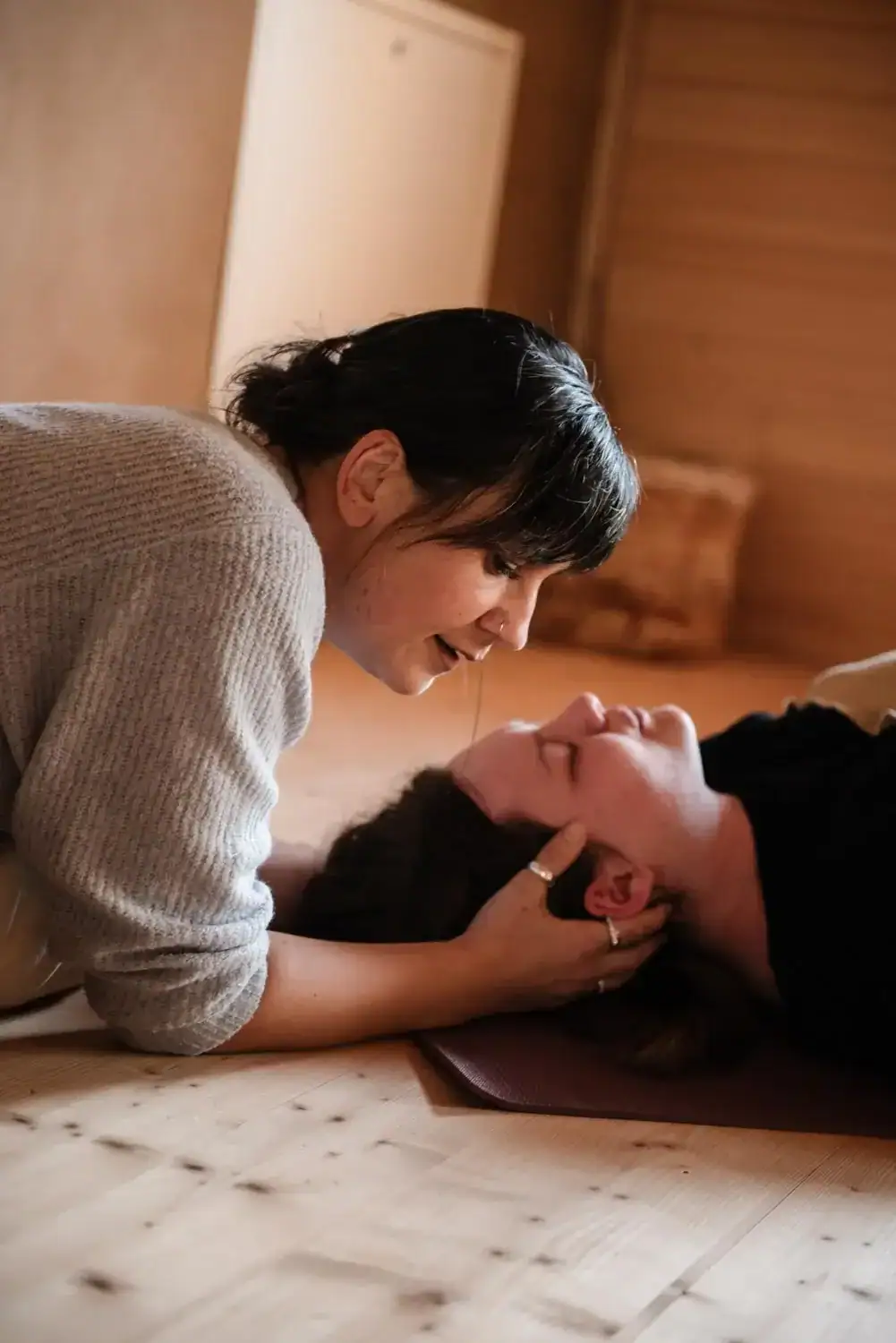 Eine Frau stützt sanft den Kopf einer anderen Frau während einer beruhigenden Atemübung in einem Haus.