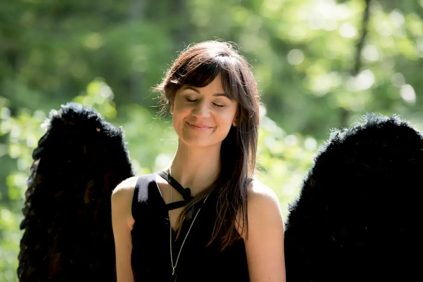 Frau mit schwarzen Engelsflügeln lächelt im Freien im Sonnenlicht.