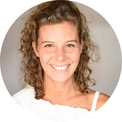 Lächelnde Frau mit lockigem braunem Haar in einem weißen Oberteil, das den Stil der Frauenbegleitung zeigt.