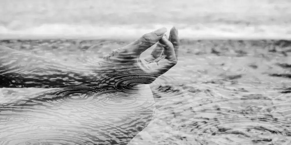 Eine Hand in Meditationshaltung mit Regentropfen, die den Selbstschutz der Frauen symbolisieren, in schwarz-weiß.