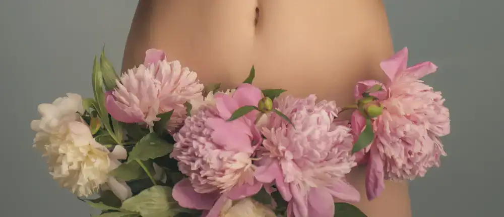 Die nackte Taille einer Frau mit rosafarbenen Blumen an den Hüften, die die Menstruation symbolisieren.