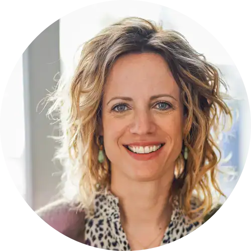 Frau mit gewelltem blondem Haar, lächelnd, trägt ein gepunktetes Oberteil, perfekt für Frauenbegleitung.