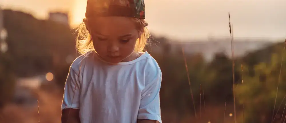 Ein kleines Kind in weißem Hemd und Mütze steht auf einem sonnenbeschienenen Feld und symbolisiert Selbstverwirklichung.