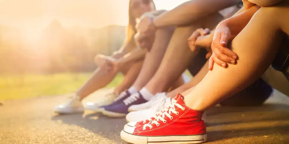 Vier Personen sitzen im Freien im Sonnenlicht, Beine sichtbar - Teenager begleiten in knallroten Turnschuhen.